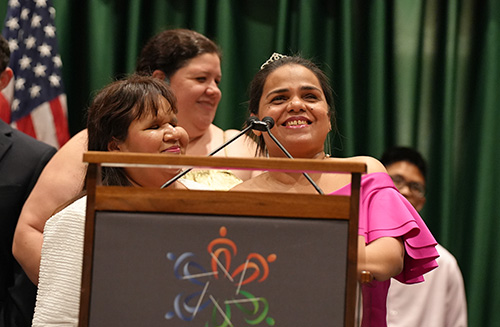 Thelma L. Gonzalez Santana smiles widely as she addresses the NFB National Convention with her translator Hilda Hernandez beside her.